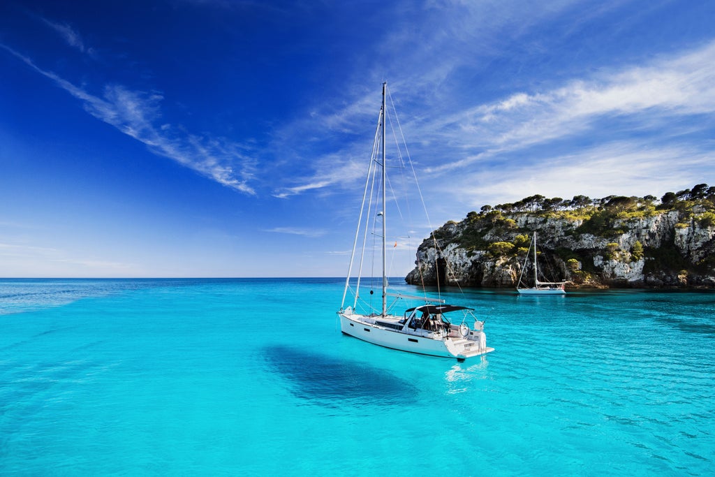 Luxurious white yacht sailing crystal-clear turquoise waters of Mallorca, with sun-drenched coastline and rocky cliffs in background