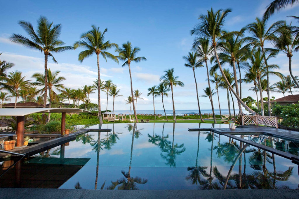 Oceanfront infinity pool surrounded by palm trees and luxury cabanas at sunset, merging with Pacific Ocean views in Hawaii