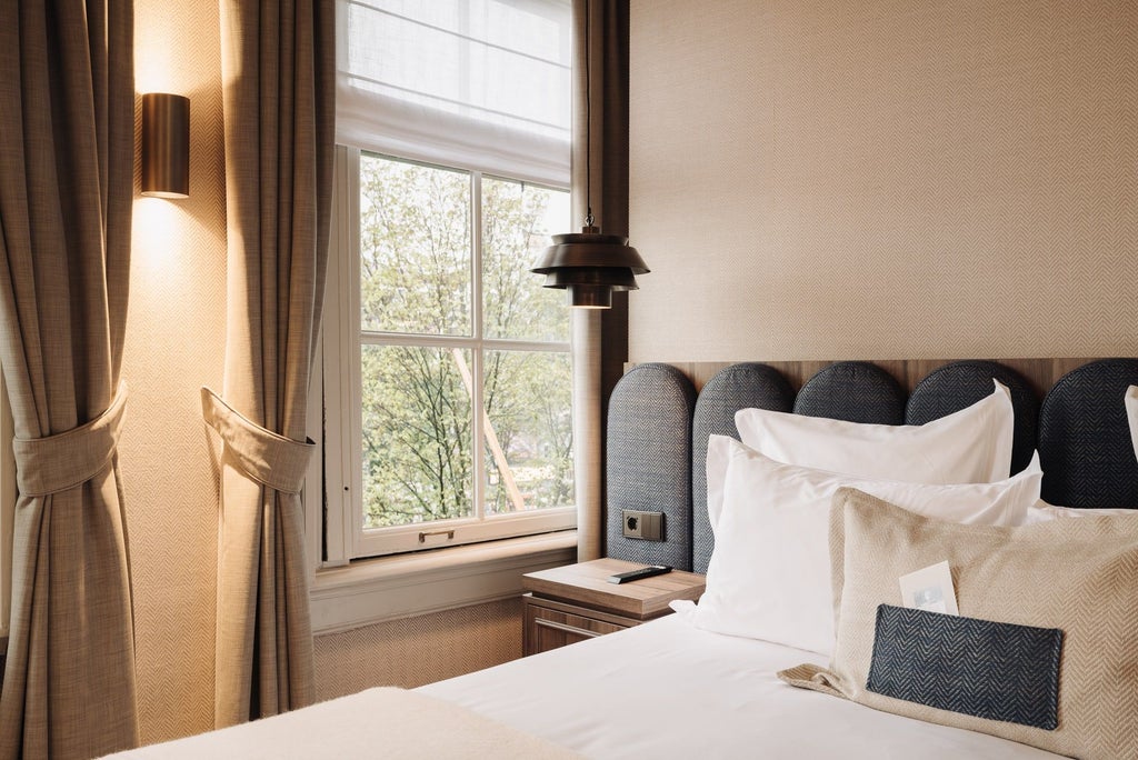 Elegant hotel room with plush bedding, modern furnishings, large windows overlooking Dutch cityscape, warm neutral tones, and sophisticated luxury design elements