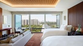 Luxurious deluxe hotel room at The Peninsula Tokyo featuring minimalist Japanese design, crisp white bedding, and city skyline view through large windows