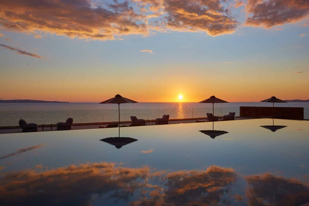 Luxurious seaside hotel with sleek white architecture, infinity pool overlooking azure Aegean waters, and minimalist Mediterranean design in coastal Greece