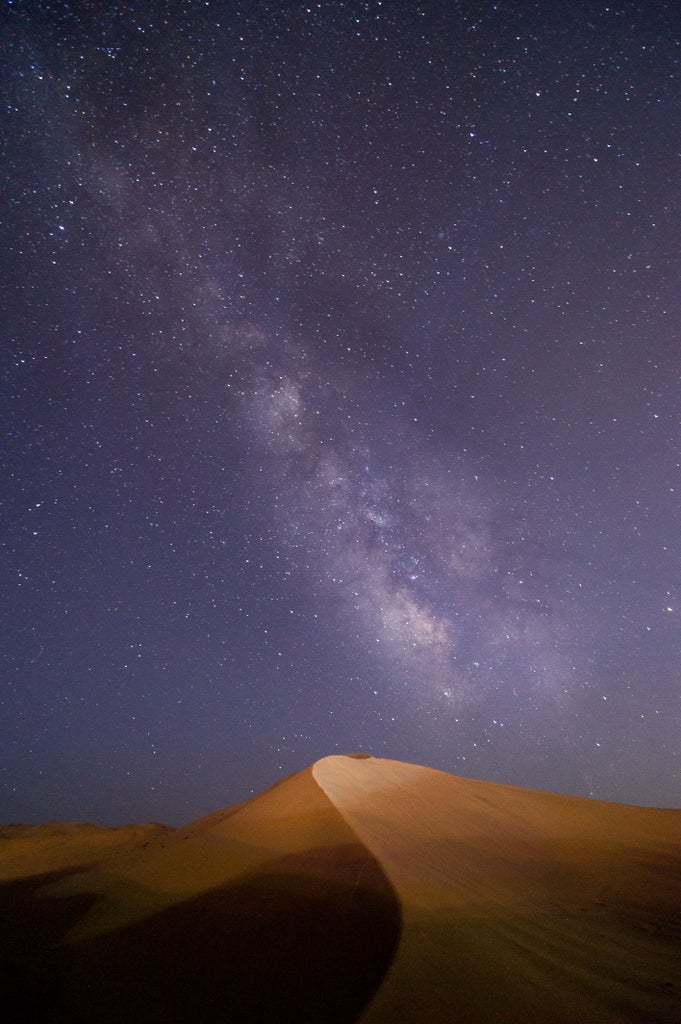 Luxurious Moroccan desert camp features white canvas tents nestled among sand dunes at sunset, with traditional lanterns lining paths