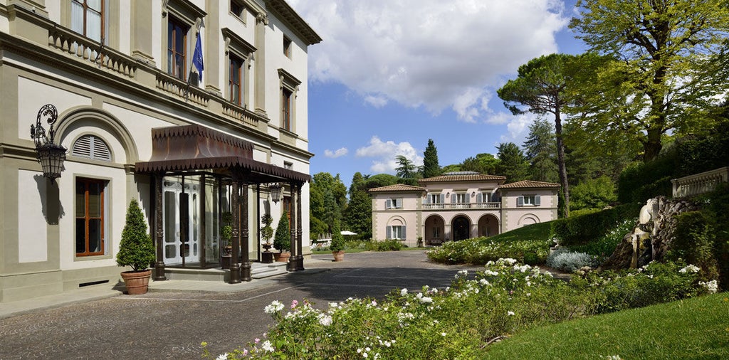 Historic Italian villa with ornate white facade, grand balconies, and manicured gardens set against Tuscan hills at golden hour