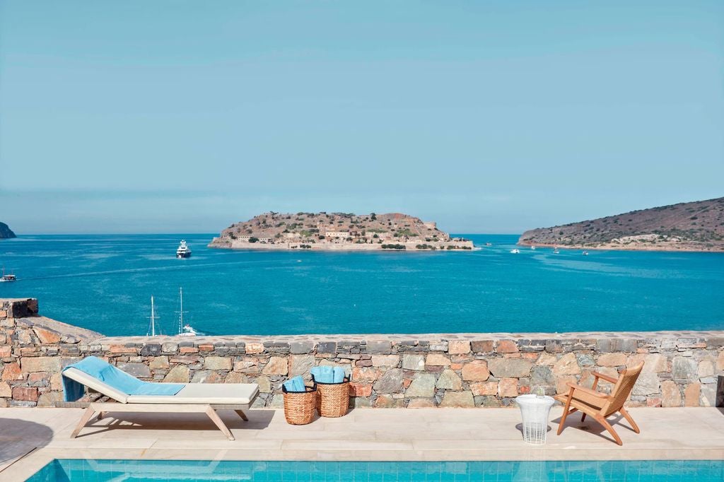 Luxurious seaside resort nestled into Greek hillside with infinity pools overlooking crystal blue Mediterranean waters and rugged coastline