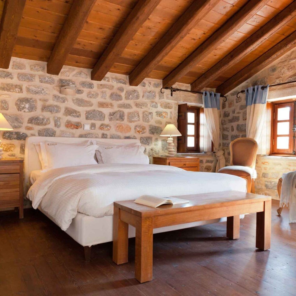 Two-level luxury suite with stone walls, wooden beams, king-sized bed, and panoramic views of the Grecian coastline at scenset Hotel