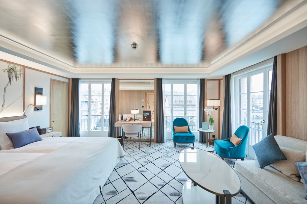 Elegant corner hotel room overlooking Zurich riverside, featuring floor-to-ceiling windows, plush king bed, and modern luxe furnishings