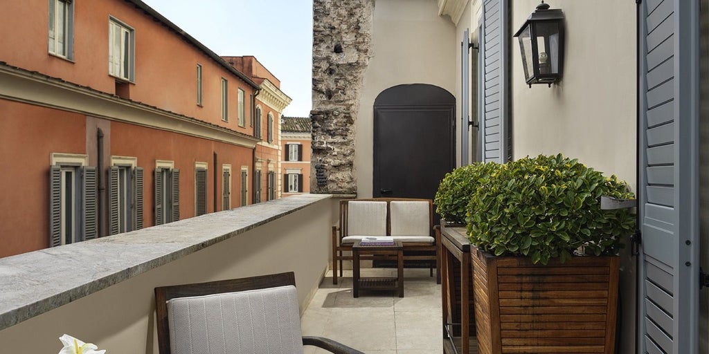 Elegant junior suite balcony at luxury hotel in Rome, featuring marble floors, designer furnishings, and panoramic view of historic Italian cityscape.