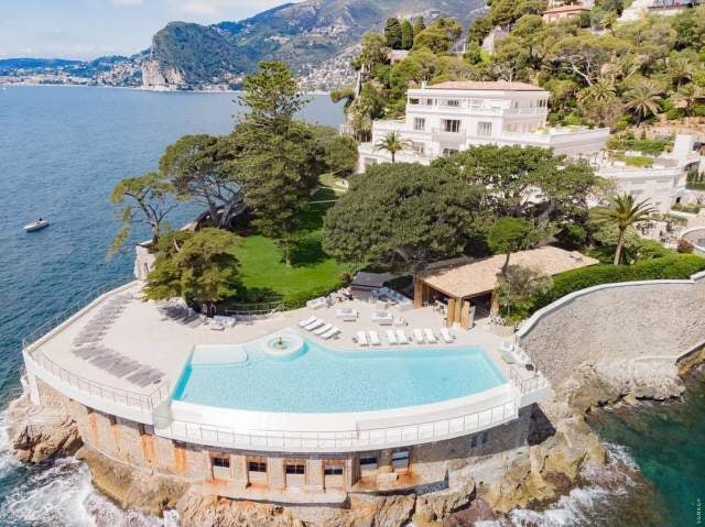 Exclusive cliffside hotel in French Riviera with infinity pool overlooking Mediterranean Sea, surrounded by manicured gardens and palms