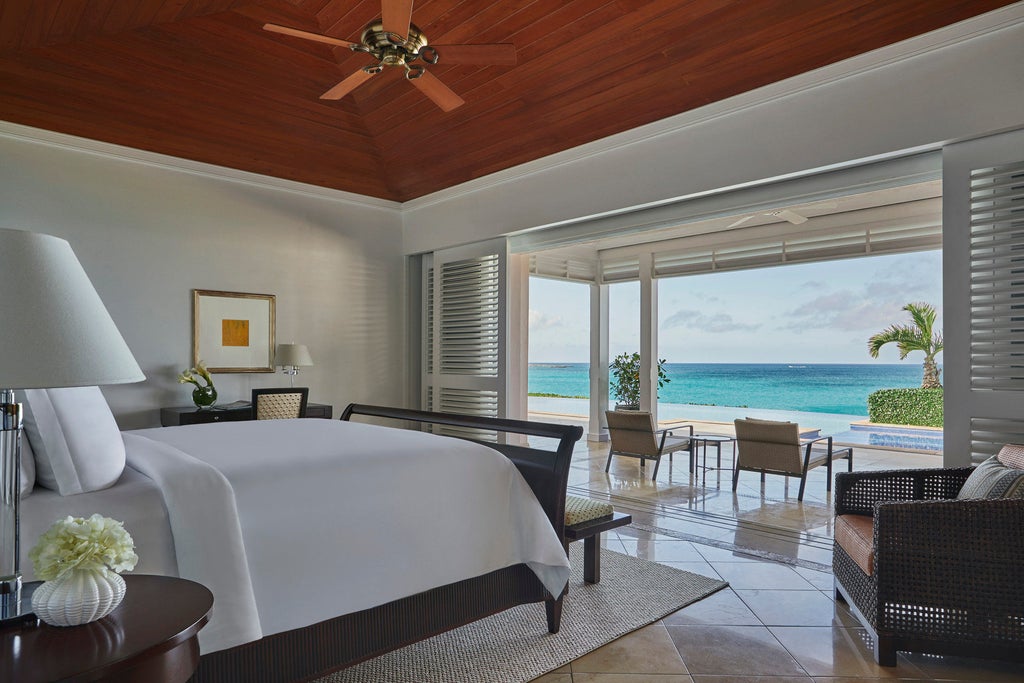 Pristine oceanfront resort with white sand beach, infinity pools, and palm trees framing luxury cabanas overlooking turquoise Caribbean waters