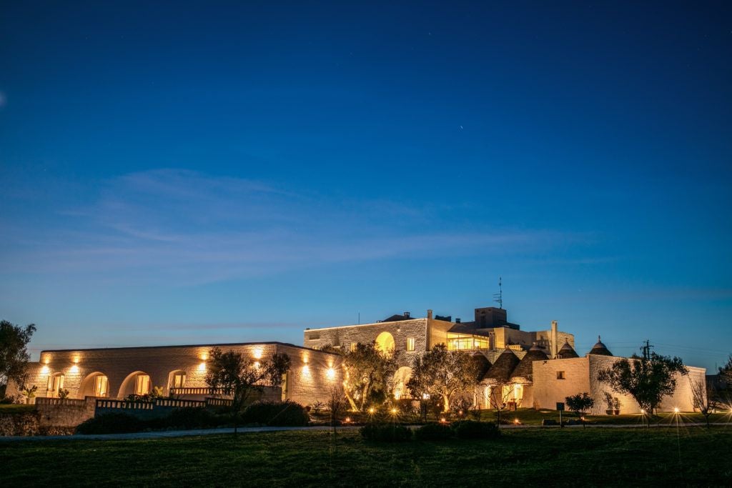 Rustic stone-walled luxury hotel Masseria Cervarolo nestled in Puglia's countryside, with elegant stone terrace and lush olive grove landscape