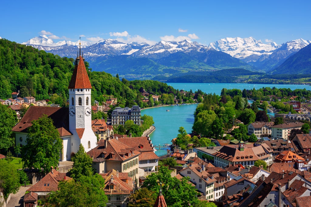 Rolling green meadows with grazing cows beneath snow-capped Alps, traditional Swiss chalet nestled in valley, wildflowers in foreground