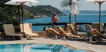 Elegant Italian coastal hotel Il Pellicano perched on rocky cliffs overlooking Mediterranean Sea, with terraced gardens and infinity pool