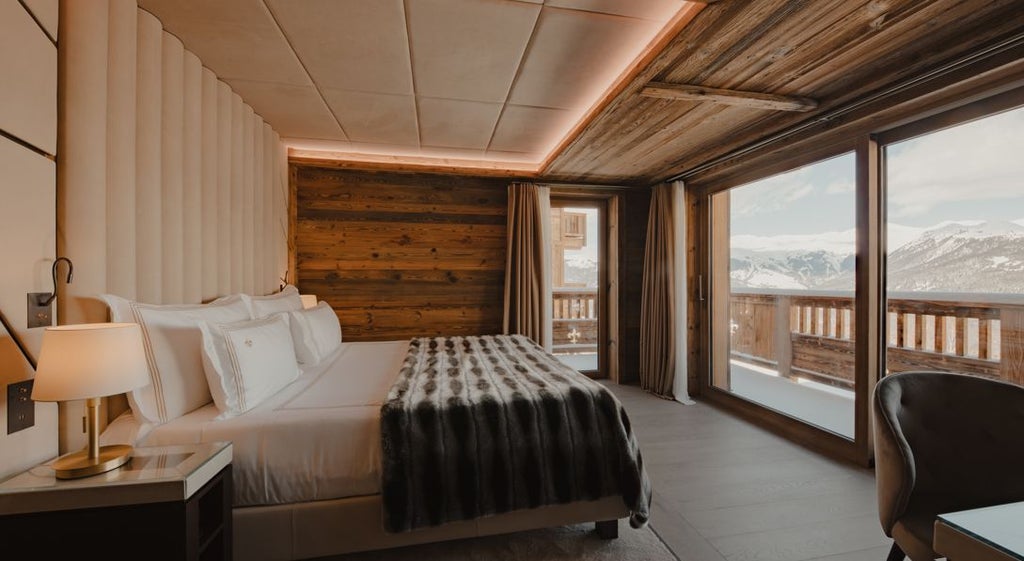 Luxurious alpine-style bedroom in Ultima Hotel Courchevel with elegant wooden accents, plush bedding, and panoramic mountain resort view