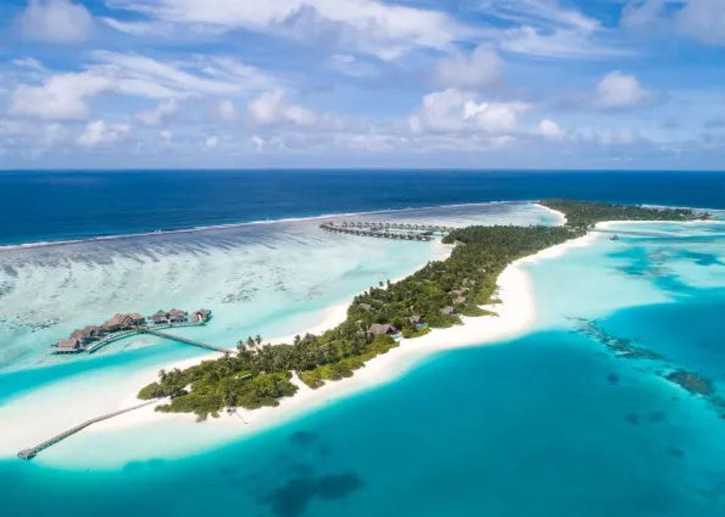 Overwater luxury villa with private infinity pool extends into turquoise Maldivian lagoon, surrounded by palm trees at sunset