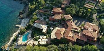 Luxurious Italian cliffside hotel overlooking Tuscan coastline, with infinity pool merging into Mediterranean Sea views at sunset