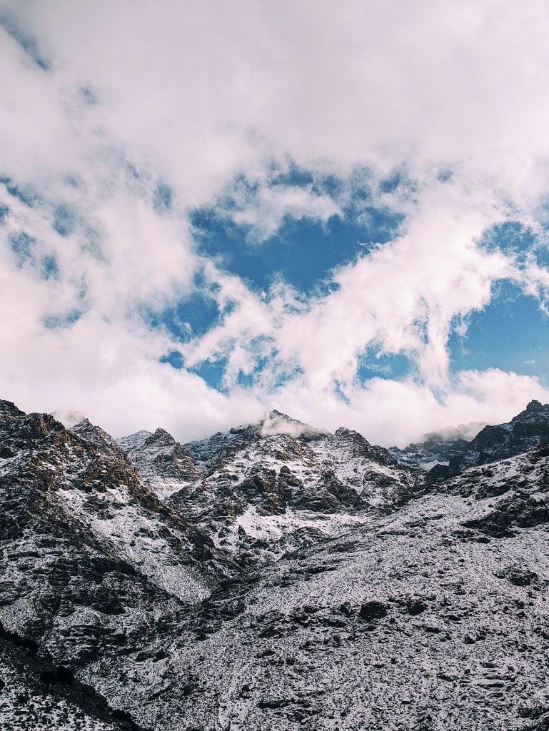 Rugged Atlas Mountains landscape with golden sunlight illuminating traditional Berber trail, hikers traversing rocky terrain with dramatic peaks and verdant valleys in Morocco