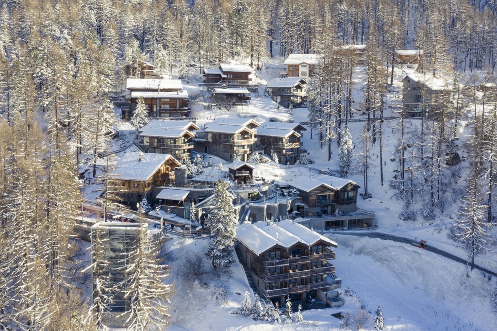 Luxurious mountain resort hotel with modern timber exterior, floor-to-ceiling windows, and snow-capped Alpine peaks in backdrop