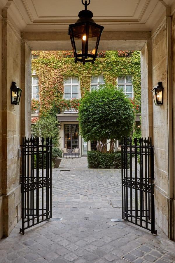 Elegant 17th-century luxury hotel entrance adorned with lush ivy, classic lanterns, and ornate iron gates in Paris's historic Marais district