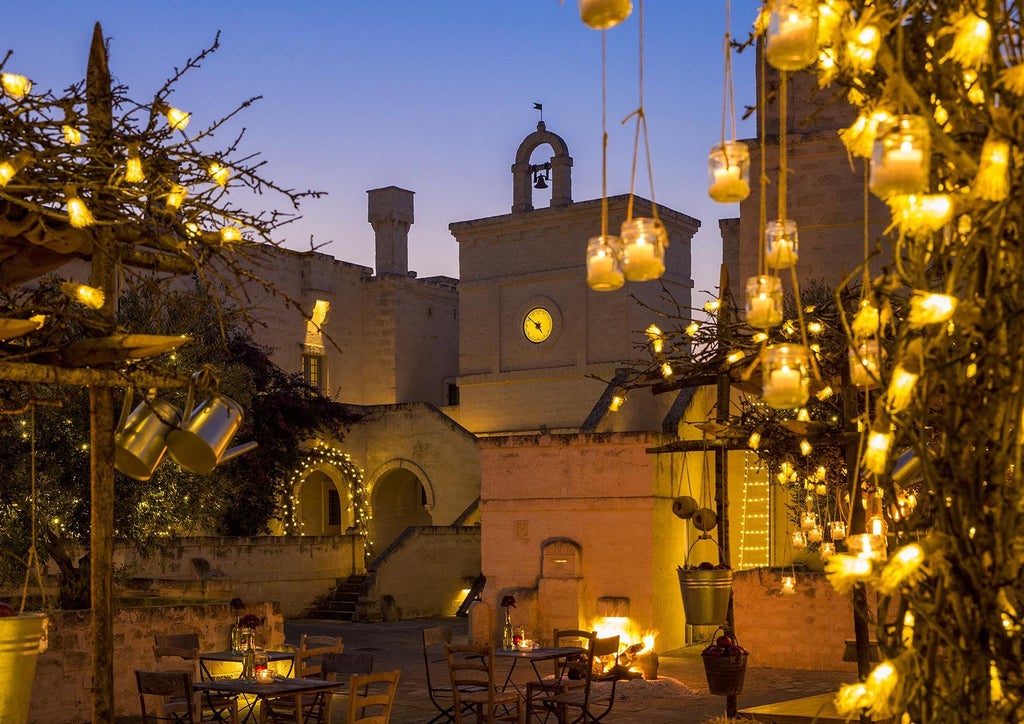 Mediterranean-style luxury hotel facade with white limestone walls, arched windows, and manicured gardens in Puglia's countryside at sunset