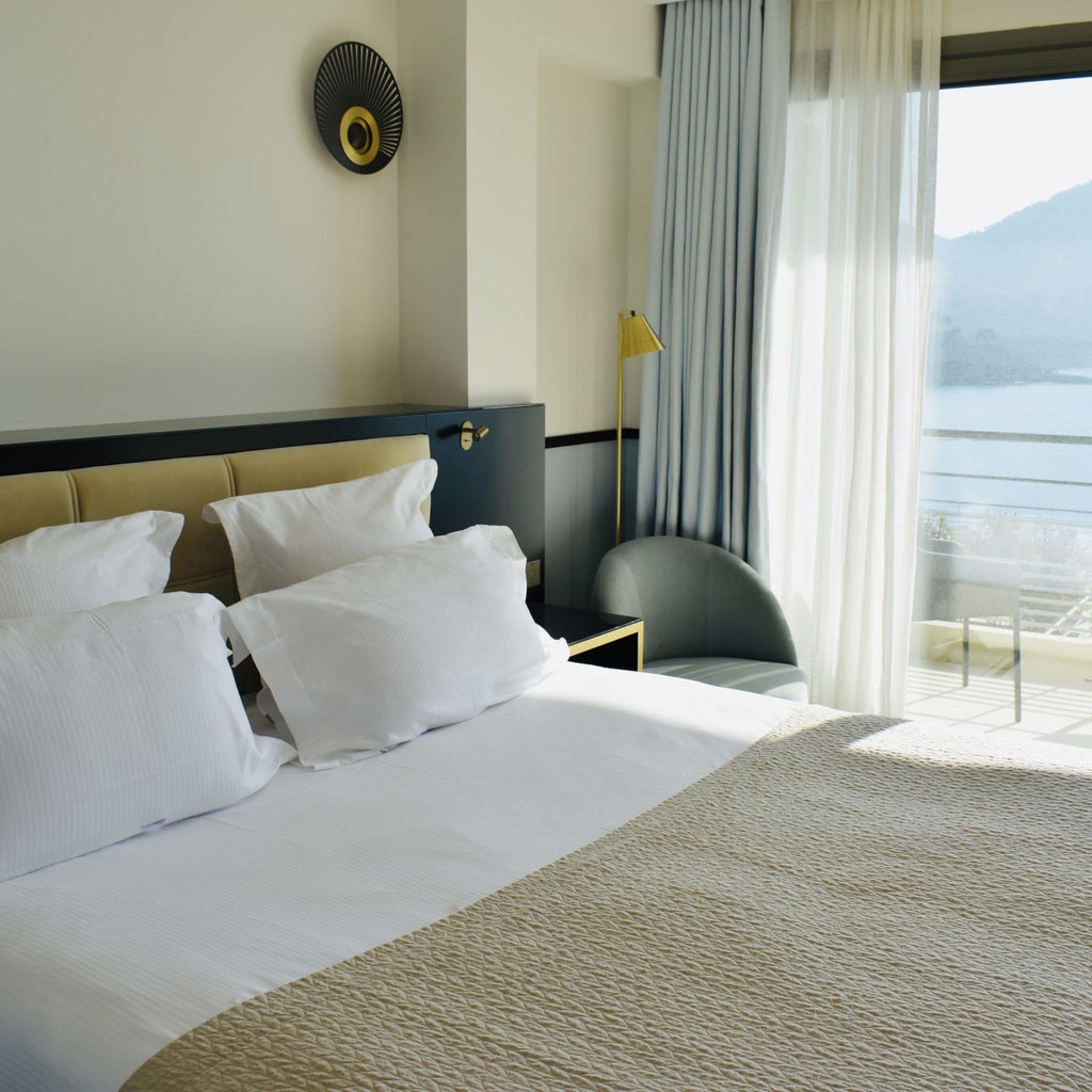 Elegant hotel room with panoramic Mediterranean views, featuring modern decor, king bed, and private balcony with white railing