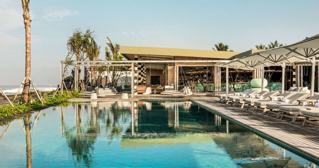 Modern beachfront resort with tiered infinity pools overlooking Canggu surf break, featuring contemporary white architecture and palm trees