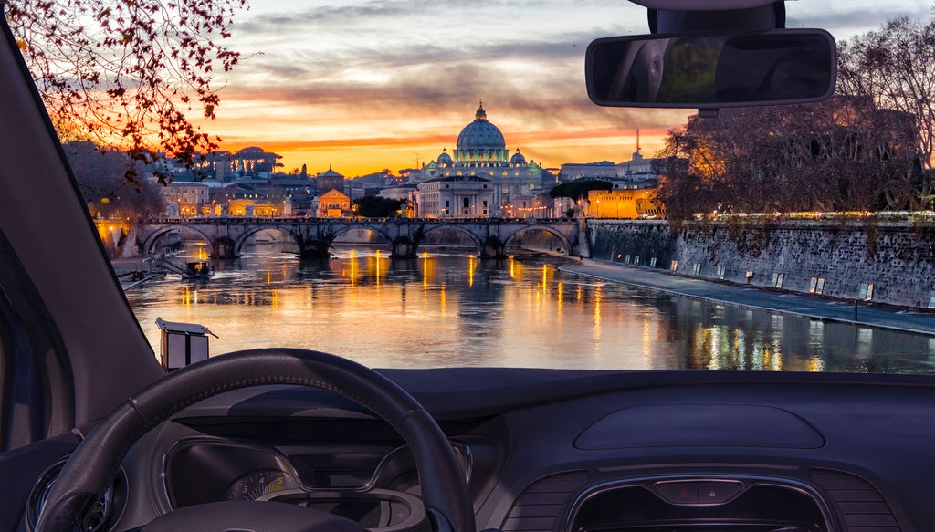 Vintage red Fiat 500 car touring illuminated Roman streets at night, passing iconic landmarks like the Colosseum and lit fountains