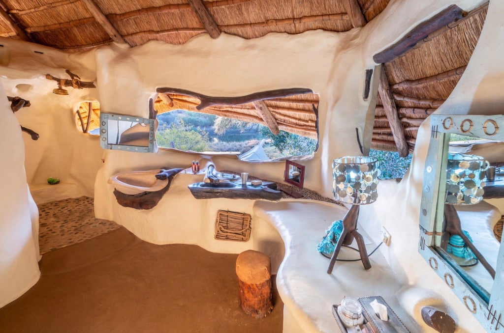 Luxurious safari lodge with curved thatched roof overlooking Zambezi River, featuring open-air living spaces and natural stone walls