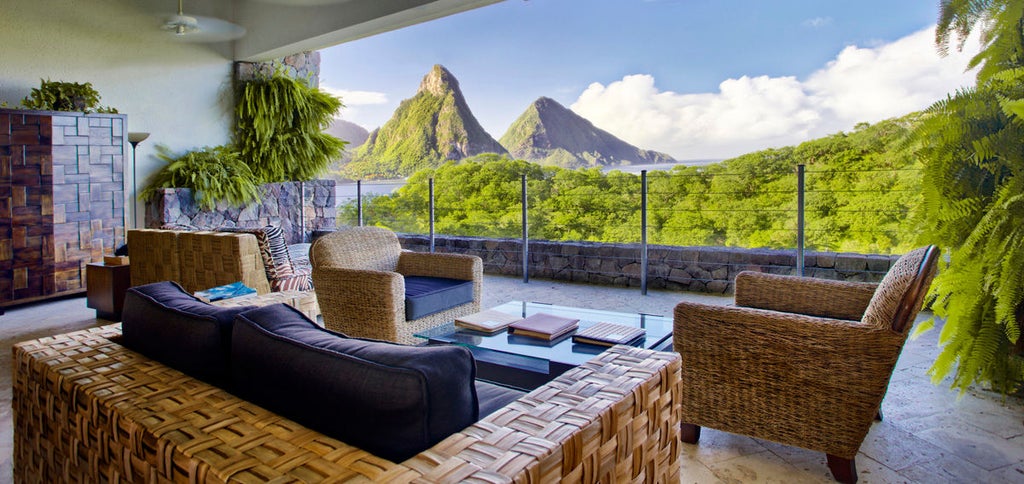 Infinity pool merges with Caribbean Sea views at luxury resort, featuring stone columns and open-air suite with curved architecture