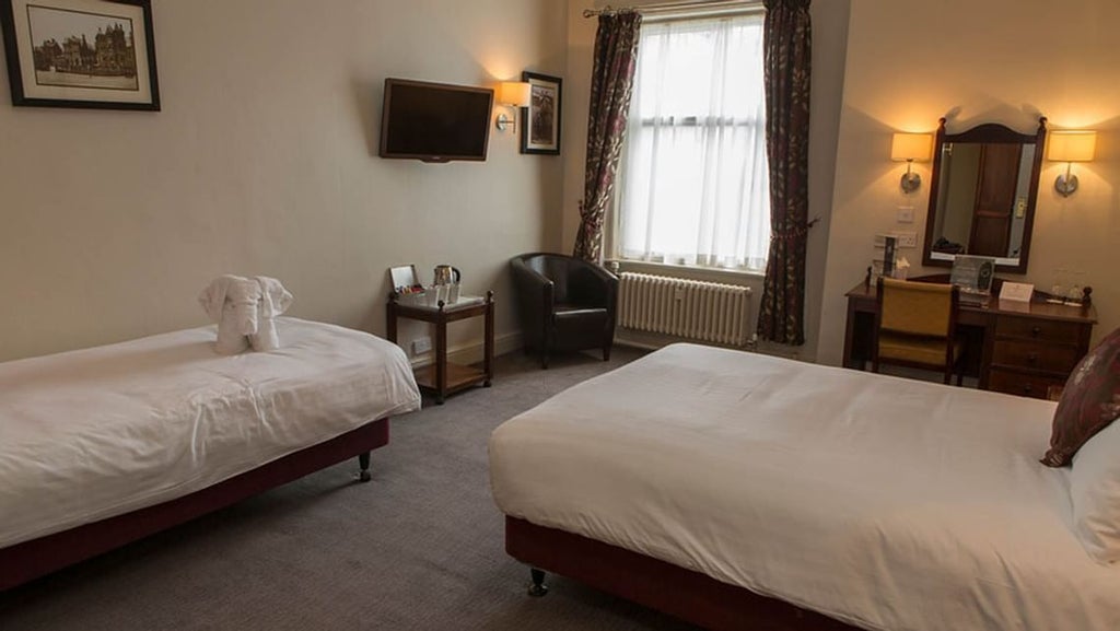 Spacious family hotel room with modern decor, plush king-sized bed, elegant wooden furnishings, and large window overlooking scenic UK landscape at The Crown Hotel