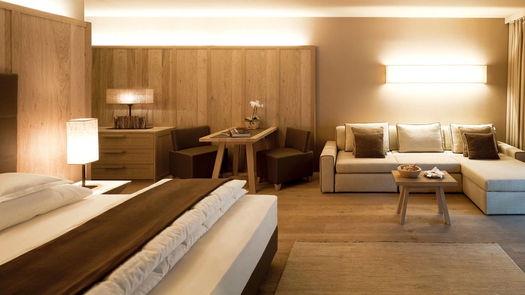 Modern mountain hotel room with panoramic Dolomites views, featuring wood paneling, designer furnishings, and floor-to-ceiling windows