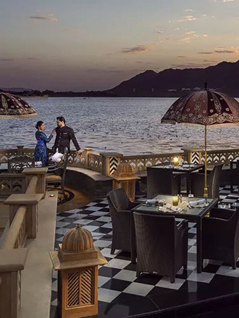 Opulent lakeside palace hotel with ornate domes and archways reflecting in Lake Pichola at golden hour, white marble facade glowing