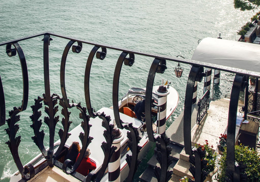 Opulent hotel suite featuring a grand king bed with ornate headboard, antique Venetian furnishings, and private terrace overlooking gardens