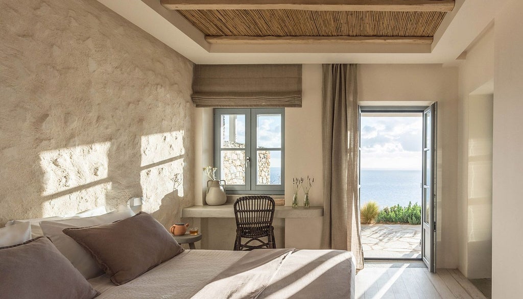 Minimalist white Cycladic hotel room with panoramic Aegean Sea view, clean lines, elegant white furnishings, and a sleek private balcony overlooking azure waters