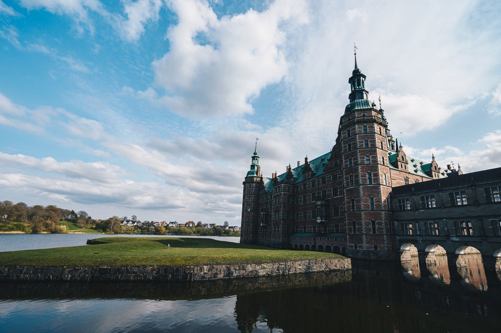 Grand Renaissance Frederiksborg Castle reflected in lake waters, with ornate copper spires and baroque architecture set in lush gardens.