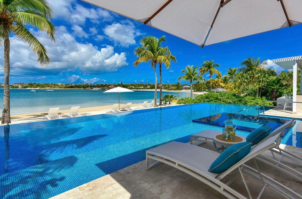 Luxurious beachfront resort with white sandy shore, crystal-clear turquoise waters, and elegant palm-lined tropical landscape in Antigua and Barbuda.