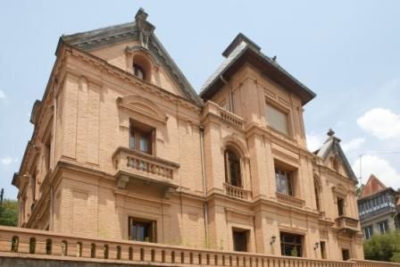 Elegant colonial-style boutique hotel with white facade, arched windows, and manicured garden framed by tropical palms in Antananarivo