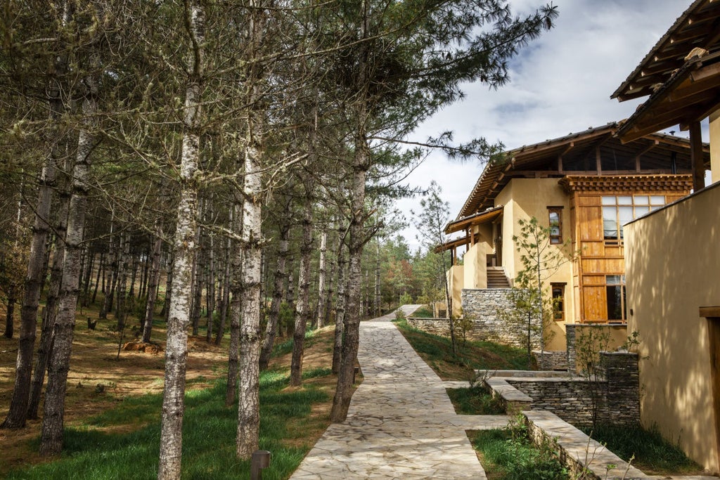 Traditional Bhutanese fortress-style lodge with stone walls and wooden details, nestled on pine-covered mountainside overlooking Paro Valley