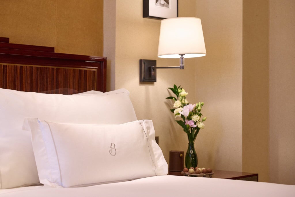 Elegant grand hotel room with plush king bed, rich dark wood furnishings, soft neutral palette, luxurious textiles at a prestigious United Kingdom accommodation