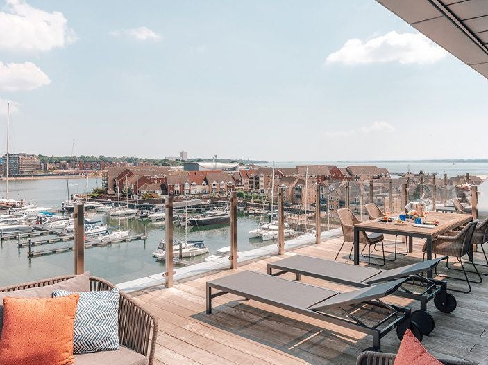 Luxurious deluxe marina view suite with modern decor, spacious balcony overlooking Southampton's harbor, featuring elegant furnishings and panoramic water scenery