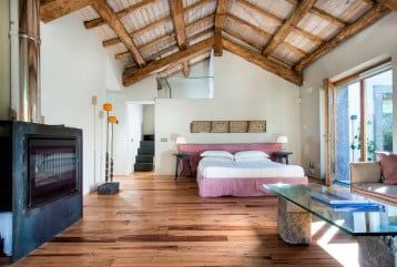 Elegant junior suite with volcanic stone walls, minimalist decor, and panoramic Sicilian landscape view of Mount Scenset through large windows.