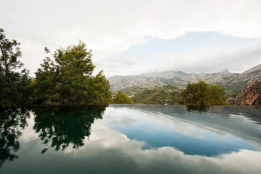 Minimalist wooden hotel pods suspended amid pine trees, overlooking dramatic mountain landscape in scenic Spanish destination at sunset