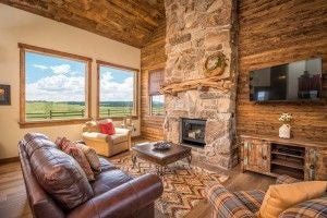 Rustic wooden interior of mountain lodge room with plush bedding, natural light, panoramic wilderness view of scenic ranch landscape near national park