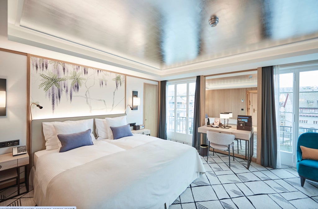 Elegant riverside corner room with wrap-around windows, plush king bed, modern furnishings, and panoramic views of Zurich's waterfront