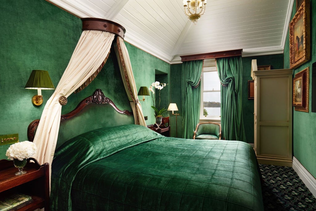 Elegant hotel room with lake views featuring period furniture, crystal chandelier, four-poster bed, and antique artwork in regal red tones