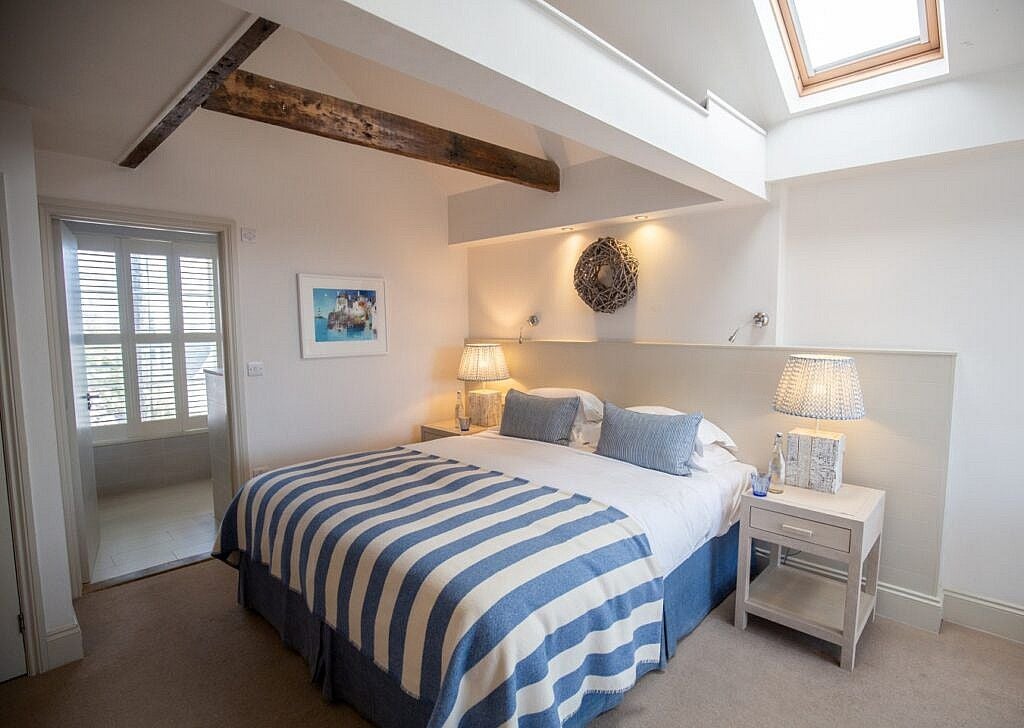 Cozy village-style hotel room with nautical blue accents, coastal view, crisp white linens, and elegant wooden furniture overlooking charming seaside scenery