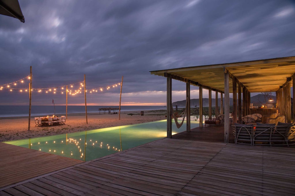 Luxurious beachfront boutique hotel with minimalist white architecture, palm trees, and infinity pool overlooking pristine Mexican coastal landscape at sunset