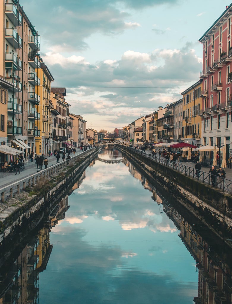 Historic Milanese street with ornate stone buildings, grand columns, and arched windows illuminated by warm evening light casting shadows