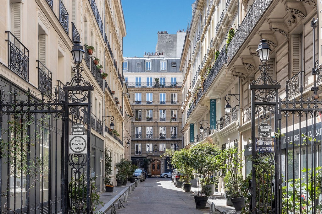 Elegant French boutique hotel with cream-colored facade, wrought-iron balconies, and lush window boxes in charming Parisian architectural style