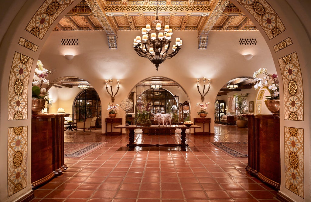 Spanish colonial-style luxury resort with white stucco walls and red-tiled roofs nestled among palm trees along the Santa Barbara coastline