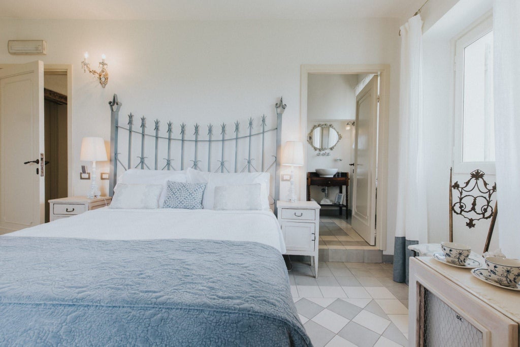 Elegant French-inspired hotel room with ornate chandelier, plush cream linens, antique wooden furniture, and soft romantic lighting in Italian villa setting